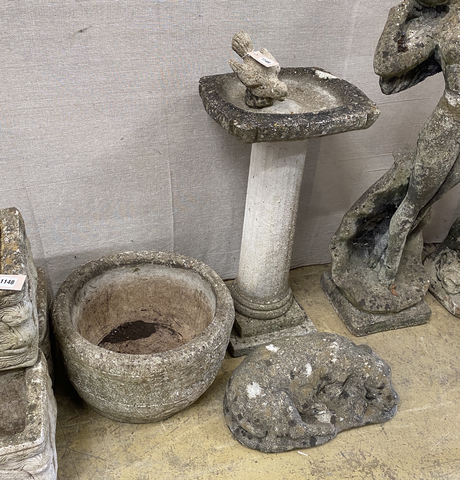 A reconstituted stone bird bath with a figure of a bird, height 70cm, a circular planter and a recumbent dog ornament